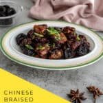 Close-up of tender Chinese braised spareribs with prunes (酸梅排骨) in a rich, glossy sauce, garnished with green onions, served in a white ceramic dish.