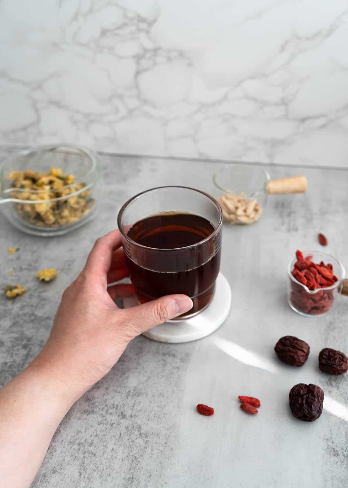 Cooling summer longan date tea in glass teacup with chrysanthemum flowers and goji berries on wooden table