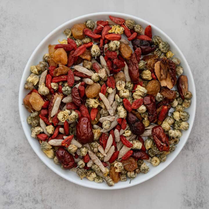 Cooling summer longan date tea in glass teacup with chrysanthemum flowers and goji berries on wooden table