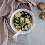 Bowl of daikon tofu kombu miso soup garnished with green onions on white background