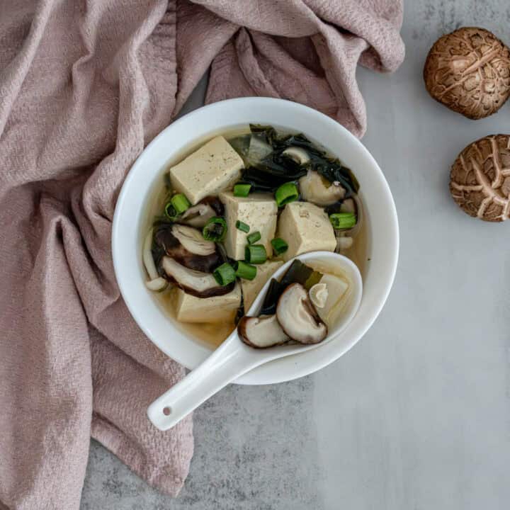 Bowl of daikon tofu kombu miso soup garnished with green onions on white background