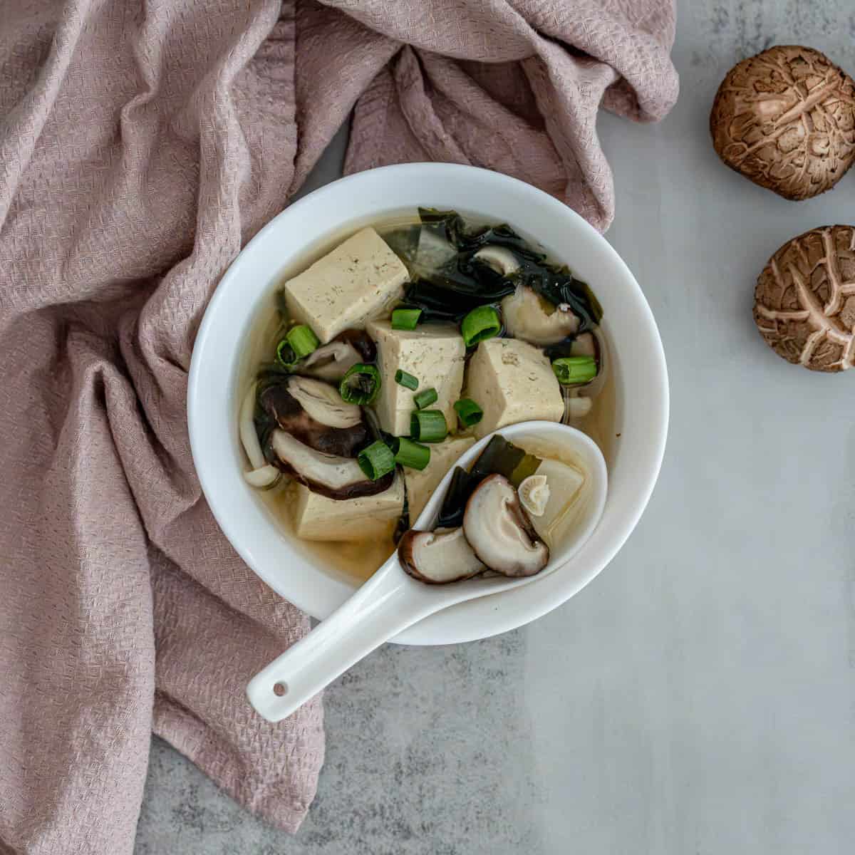 Bowl of daikon tofu kombu miso soup garnished with green onions on white background