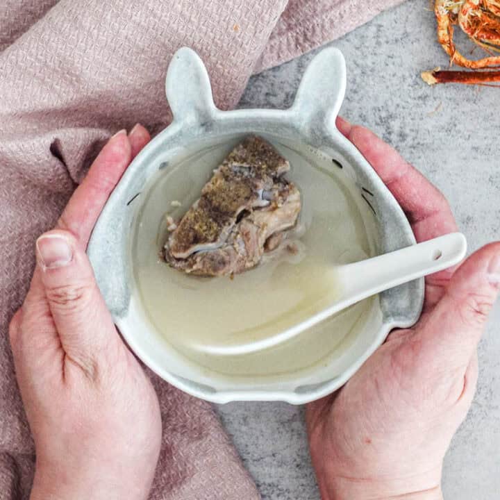 Golden TCM spring dampness soup broth poured into bowl showing hairy fig and Job's tears spleen health recipe