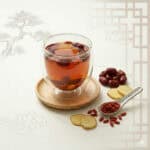 Jujube goji berry sleep tea in a double wall glass mug with dried red dates and goji berries on a dark wood surface, TCM herbal tea recipe